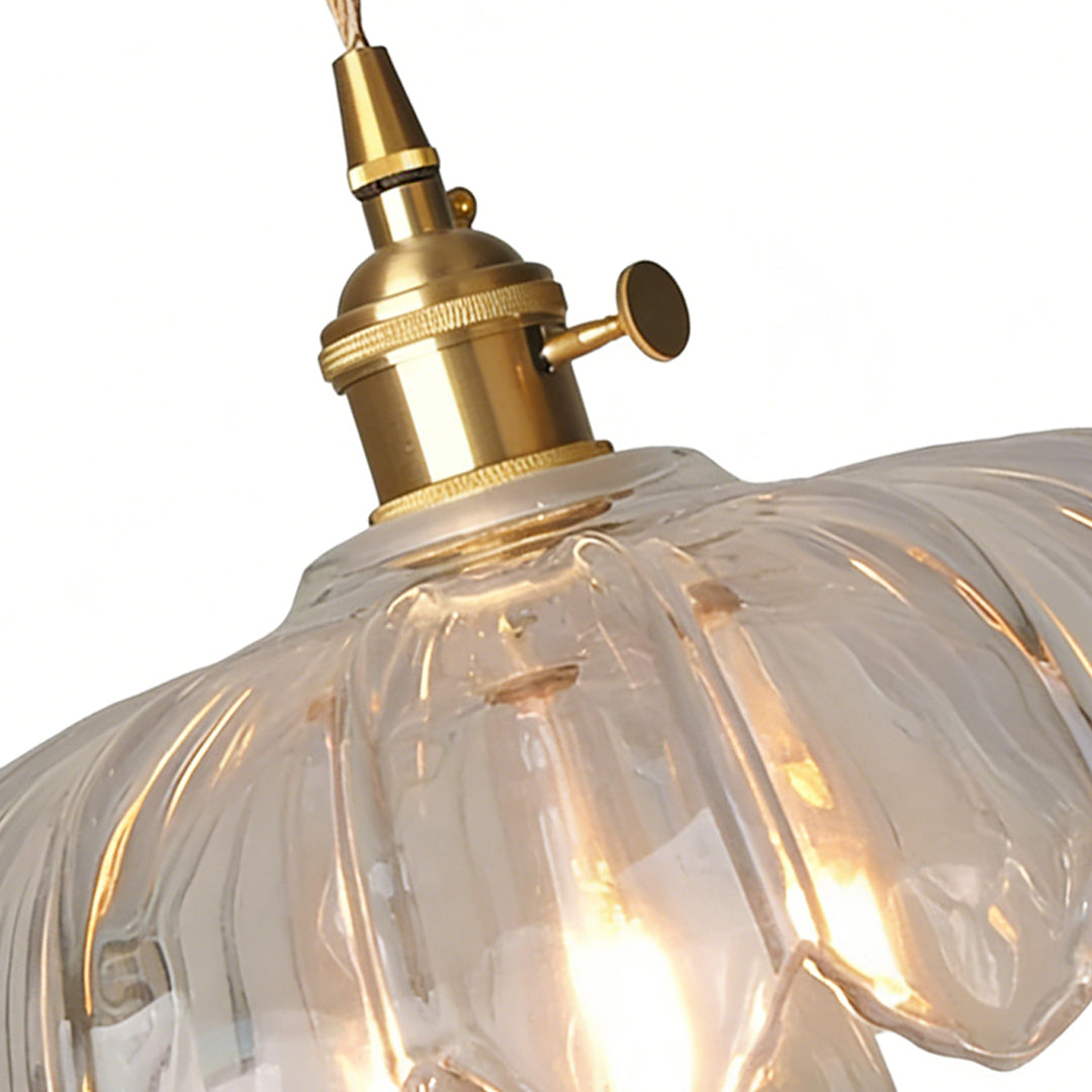 Close-up of clear glass pendant light showing thick textured glass shade and brass fitting with glowing bulb.glass-pendant-light-clear-textured-closeup