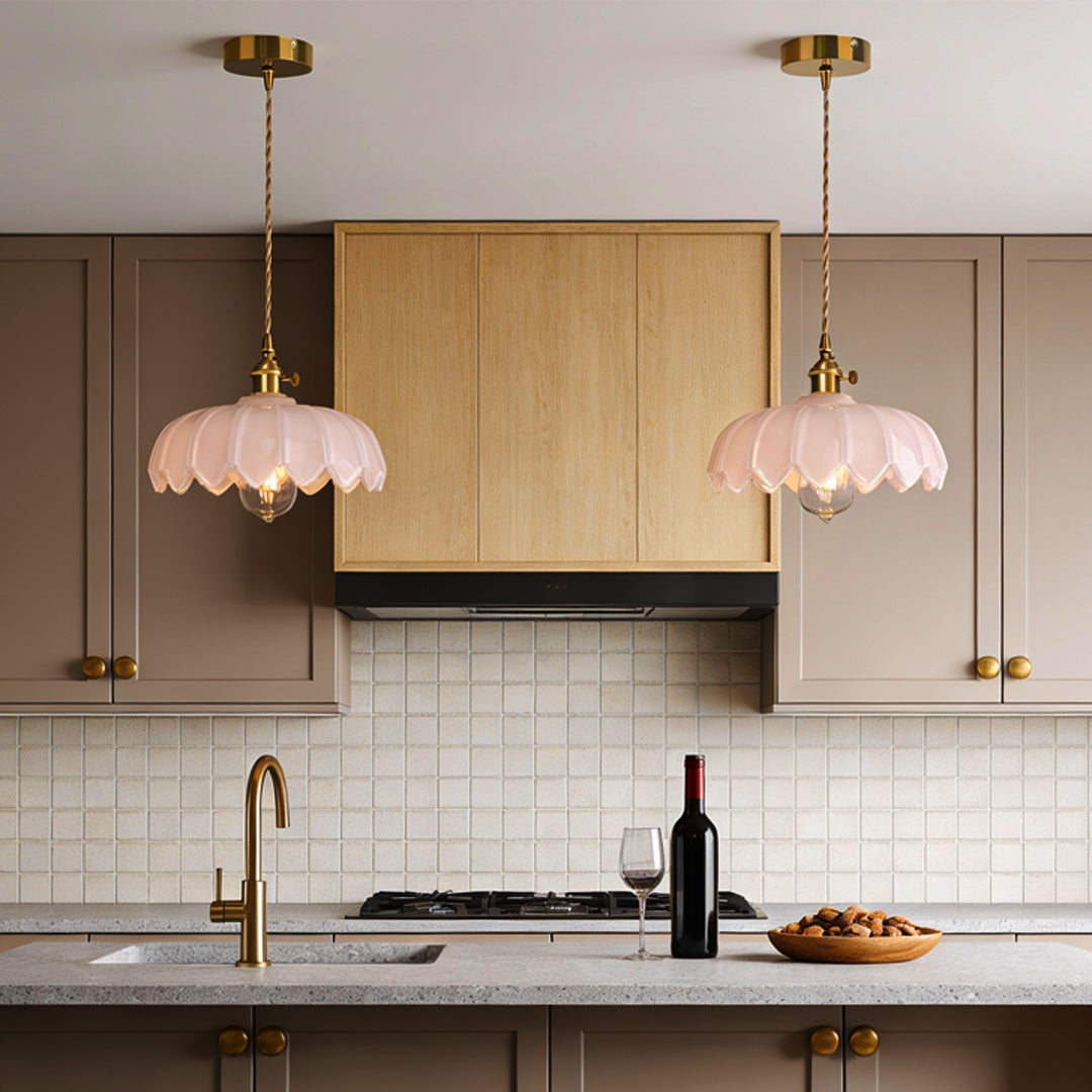 Glass pendant light with soft pink scalloped shade and brass fixture in kitchen, glowing warmly in a minimalist indoor setting.