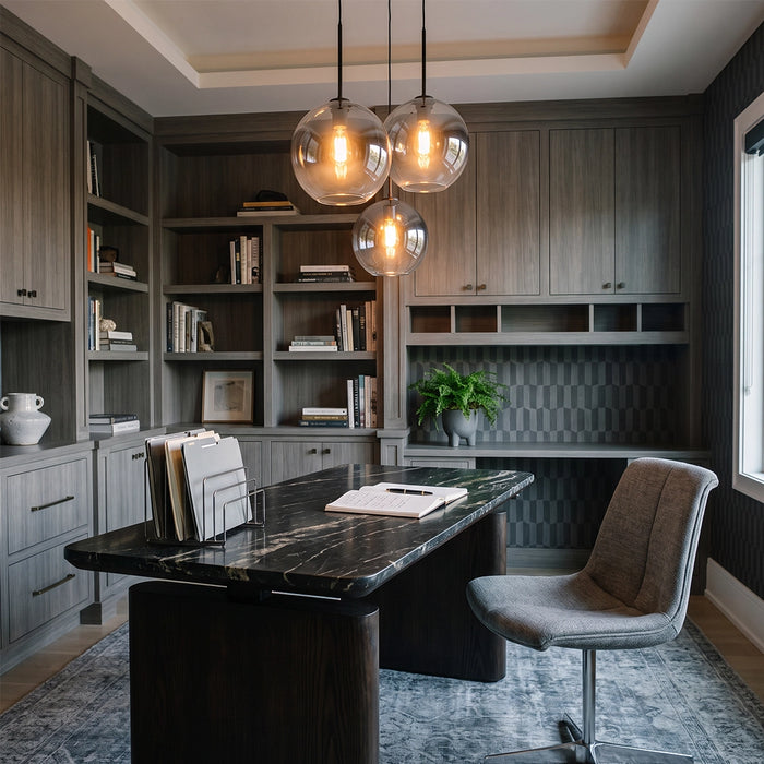 Glass round pendant lights hanging above a dark desk in a stylish home office with built-in shelving.