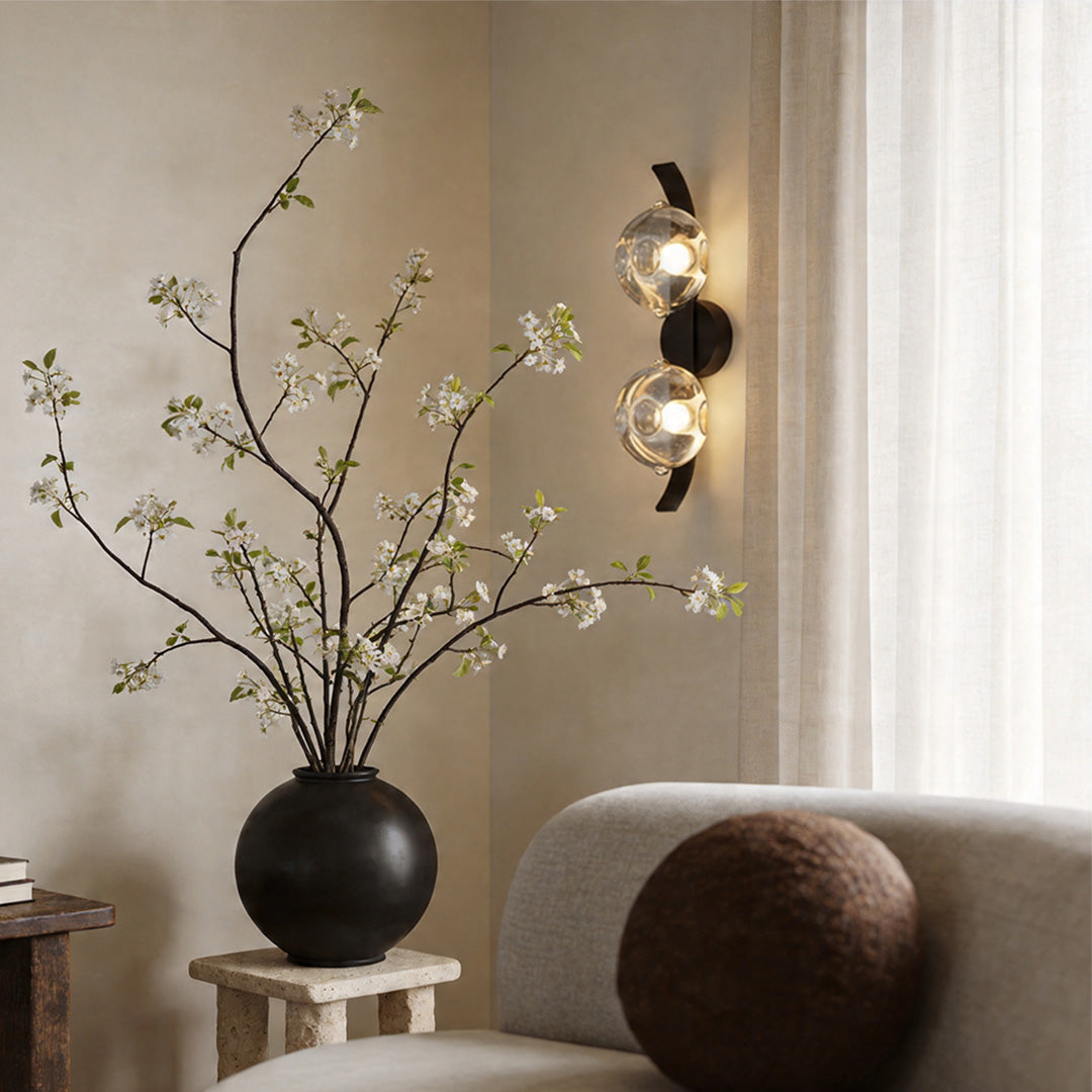 Decorative glass wall sconce with warm glow beside indoor plant.