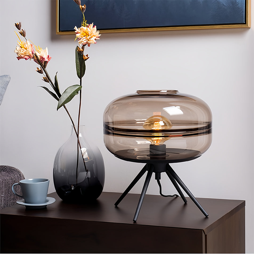 Glass small table lamp creating ambient lighting in modern bedroom with neutral decor and artistic elements