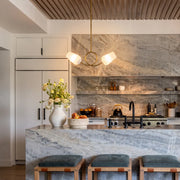 Glass vintage chandelier hanging above a marble kitchen island in a bright modern kitchen.