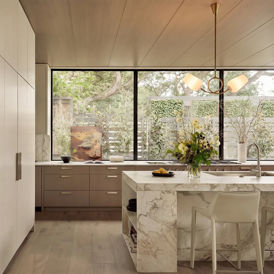 Glass vintage chandelier hanging in a modern kitchen with a large picture window and marble island.