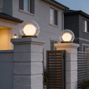 Global pillar lights with a spherical design, illuminating a modern driveway at dusk.