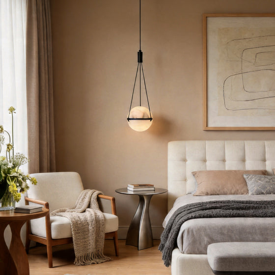 A globe pendant light fixture hanging beside a bed and cozy armchair in a warm modern bedroom.