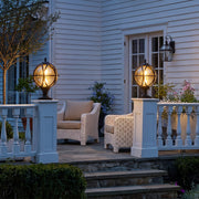 Globe pillar lights mounted on white porch columns beside a patio seating area at dusk.