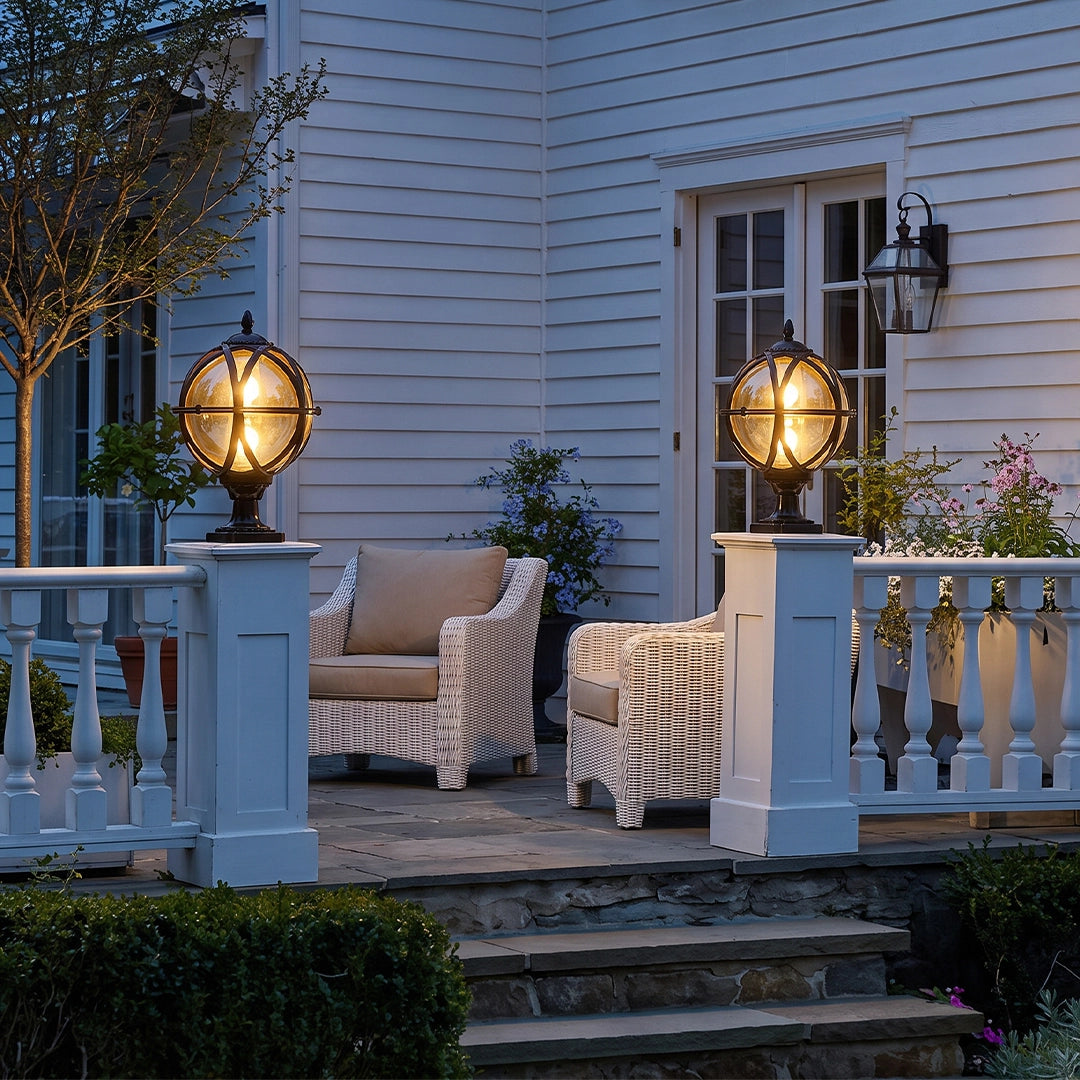Globe pillar lights mounted on white porch columns beside a patio seating area at dusk.