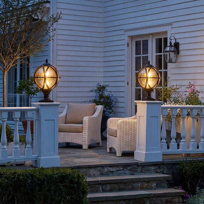 Globe pillar lights mounted on white porch columns beside a patio seating area at dusk.