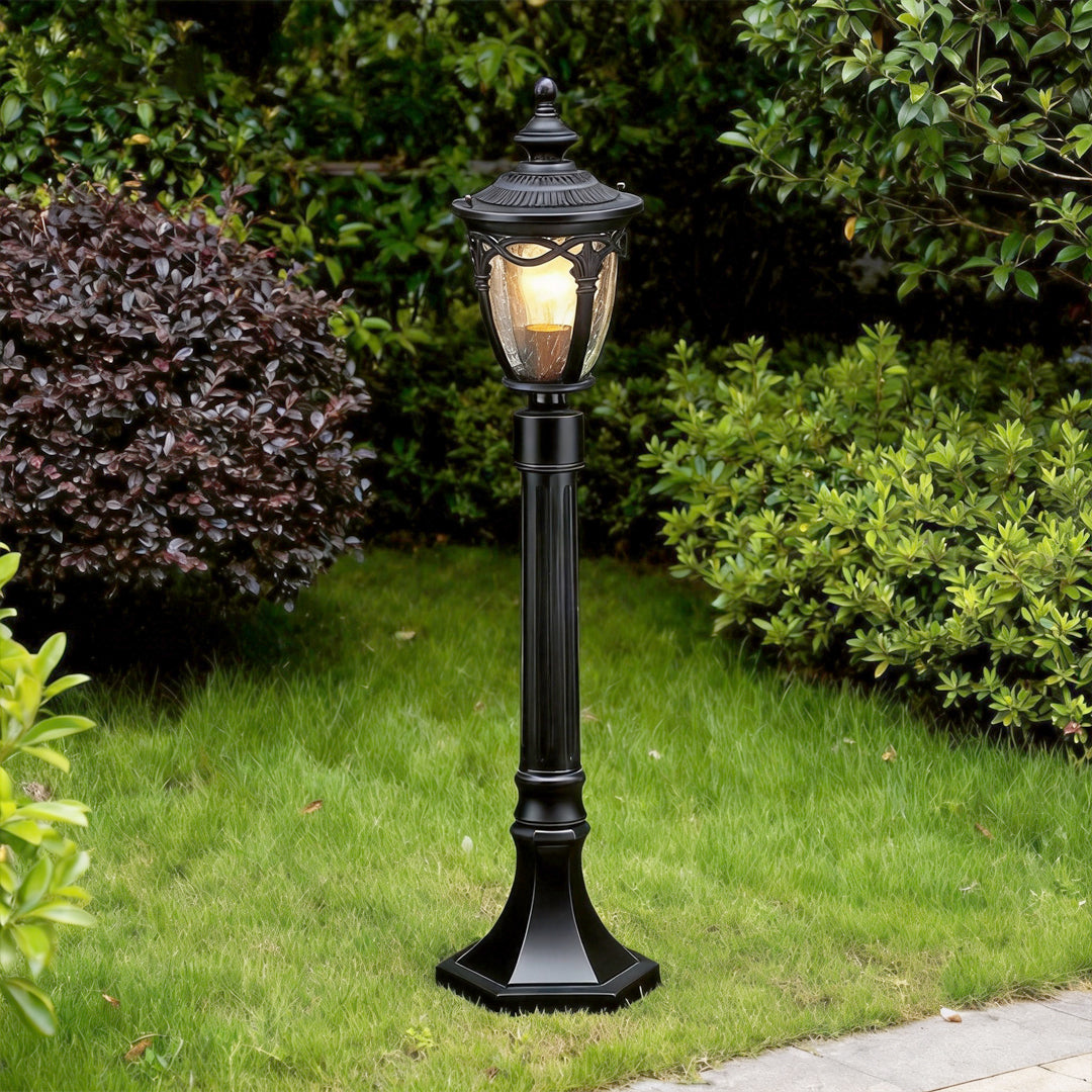 Glowing black outdoor light post standing on green grass next to a stone pathway in a garden ok