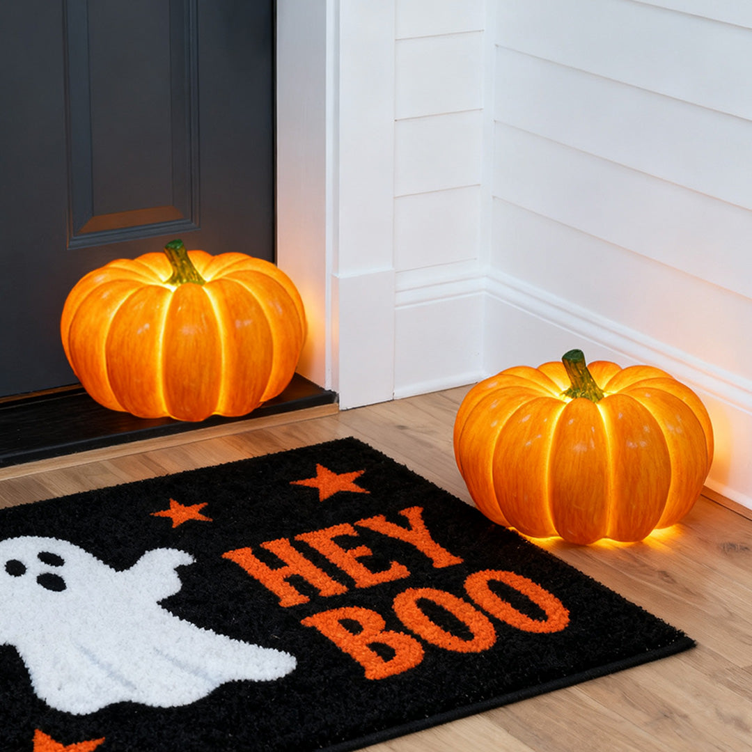 Two glowing halloween pumpkin light decorations placed on a floor next to a 'Hey Boo' doormat.