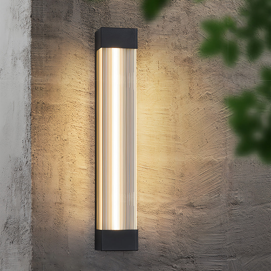 Warmly glowing linear outdoor sconce mounted on a textured concrete wall, highlighting its ribbed design.