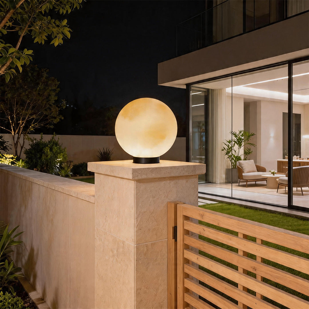 Glowing moon pillar lights mounted on stone posts at the entrance of a modern villa at night.