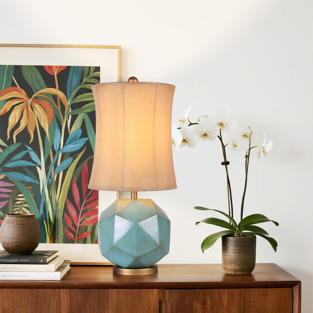 Modern industrial table lamps styled next to an orchid and a tropical plant print, highlighting the gold band and textured fabric shade.