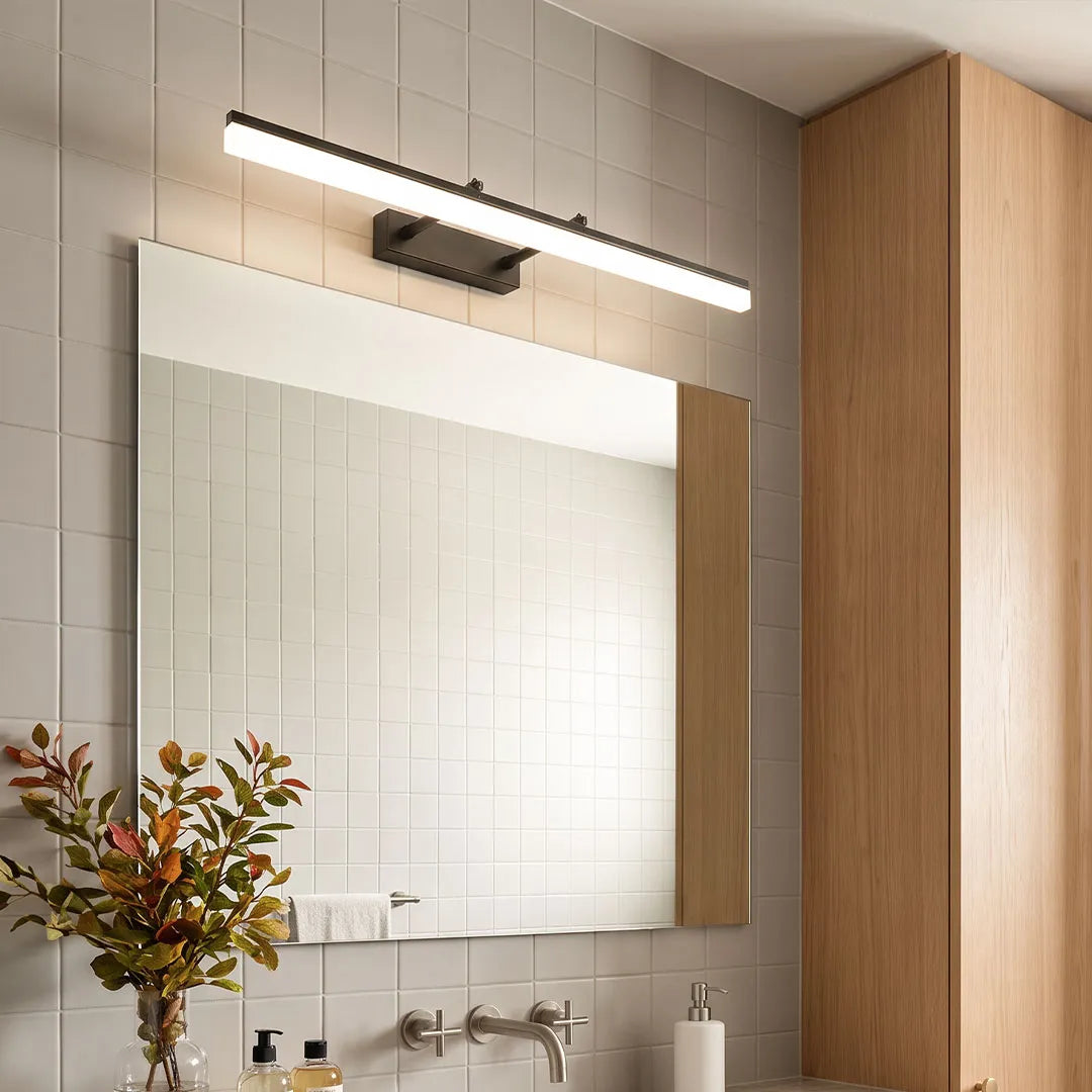 Gold bathroom vanity light bar mounted above a rectangular mirror in a modern white tile bathroom.