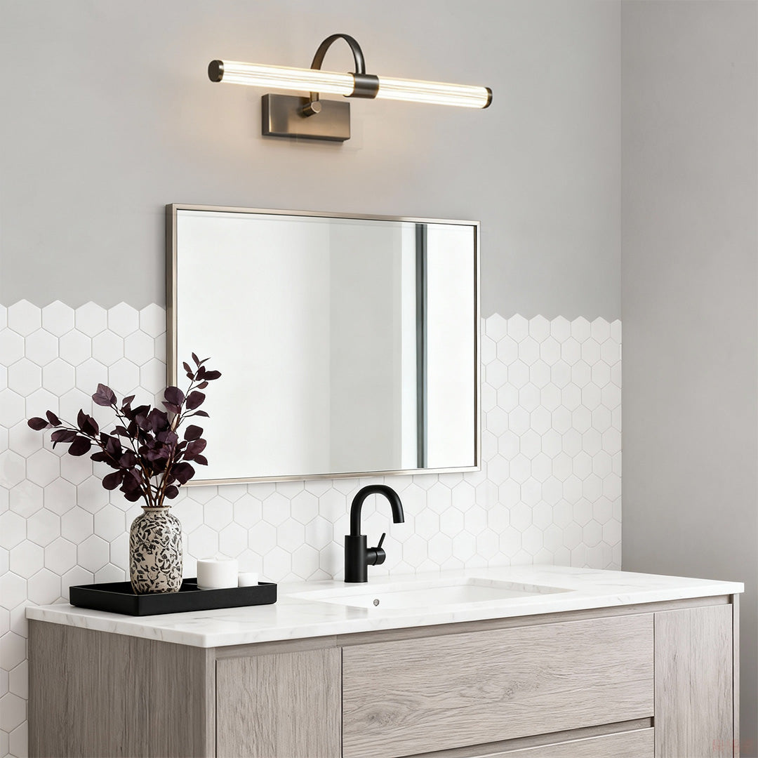 Gold bathroom vanity wall light illuminating marble bathroom with white countertop and modern fixtures.