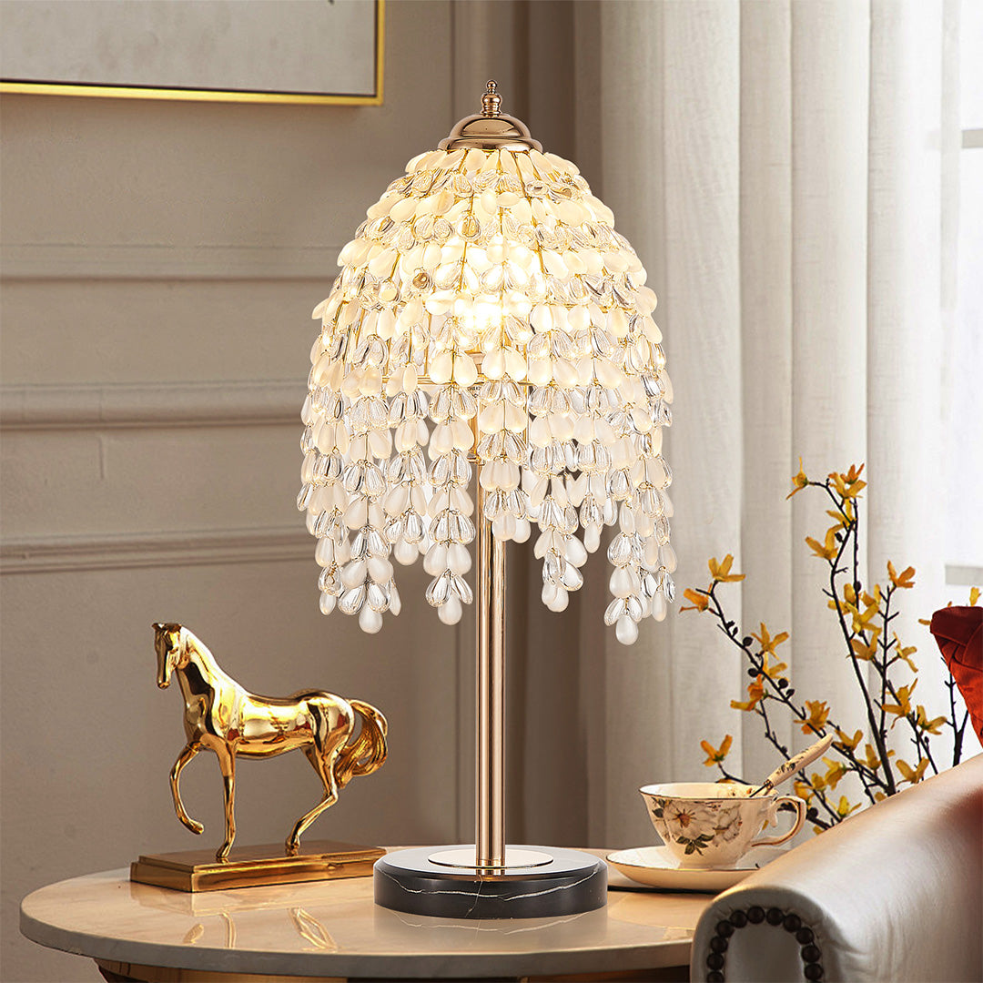 Gold bedside table lamp with glass shade chandelier inspired cascading crystal design on elegant white vanity with decorative horse statue.