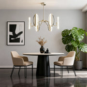 Gold chandelier modern suspended above round dining table in minimalist room with gray walls and greenery