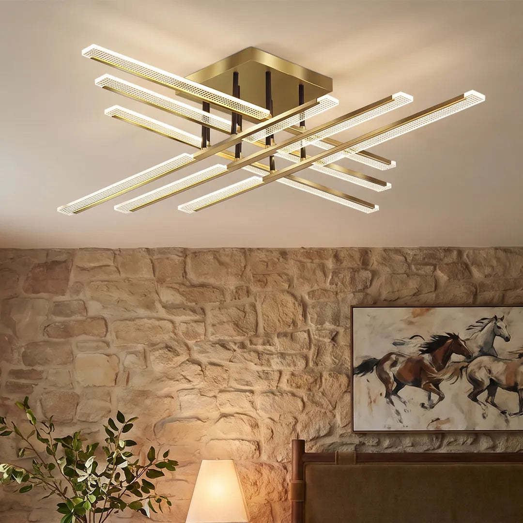 Gold cross ceiling light in a close-up view, featuring a geometric crossed linear design with crystal-style LED bars above a stone wall.