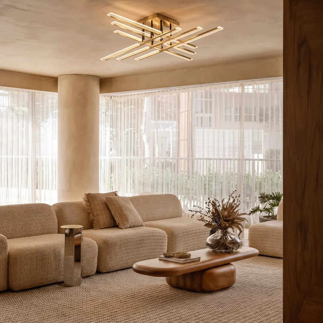 Gold cross ceiling light mounted in a bright living room with soft seating and sheer curtains.