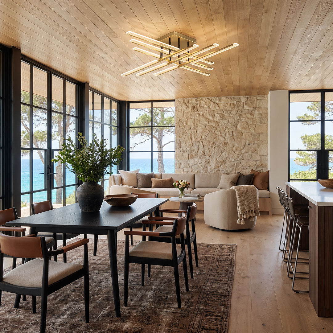 Gold cross ceiling light illuminating a modern open-concept dining and living room with a wood ceiling, stone accent wall, and large black-framed windows.