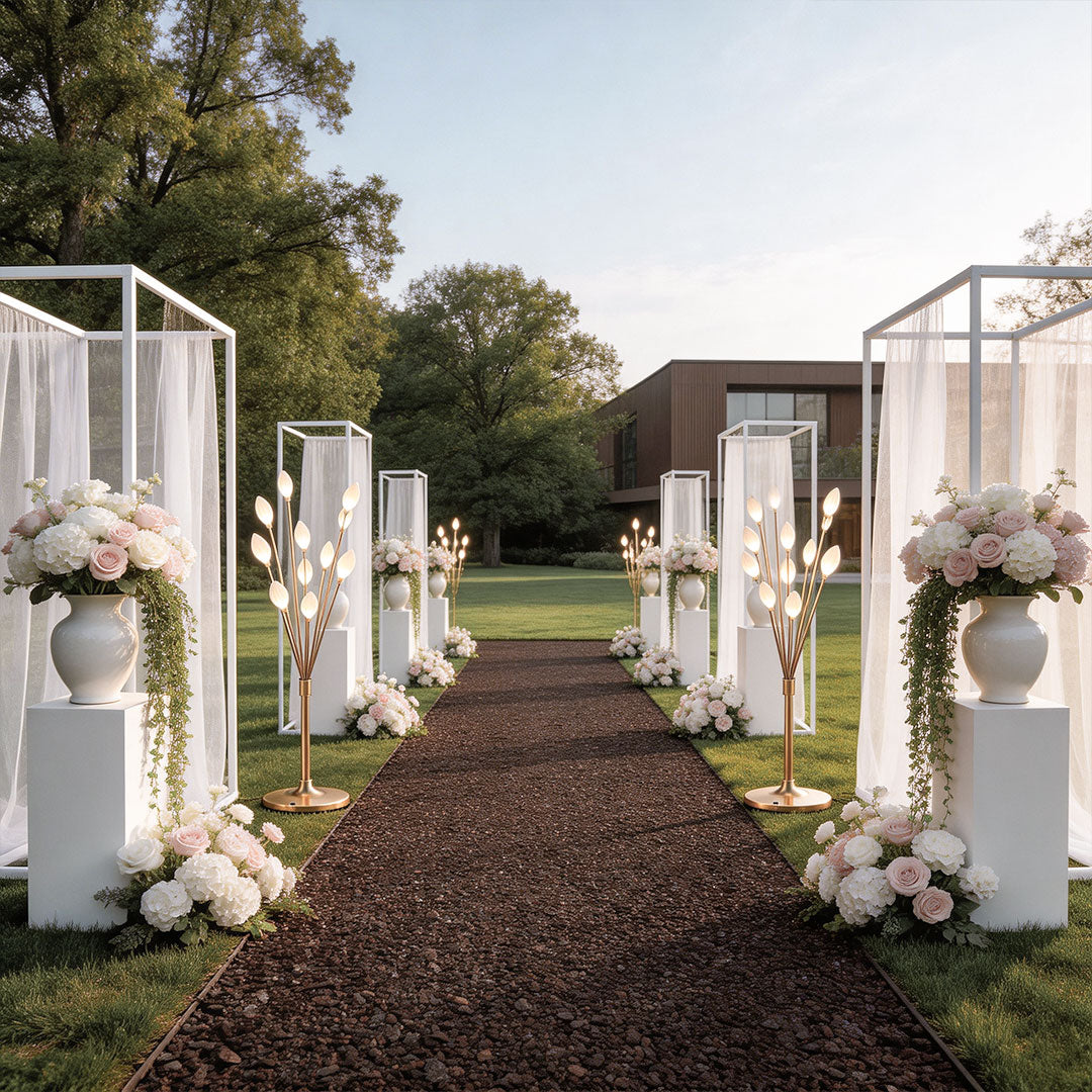 Gold decorator floor lamps lining a garden wedding aisle with white pillar frames and pink roses.