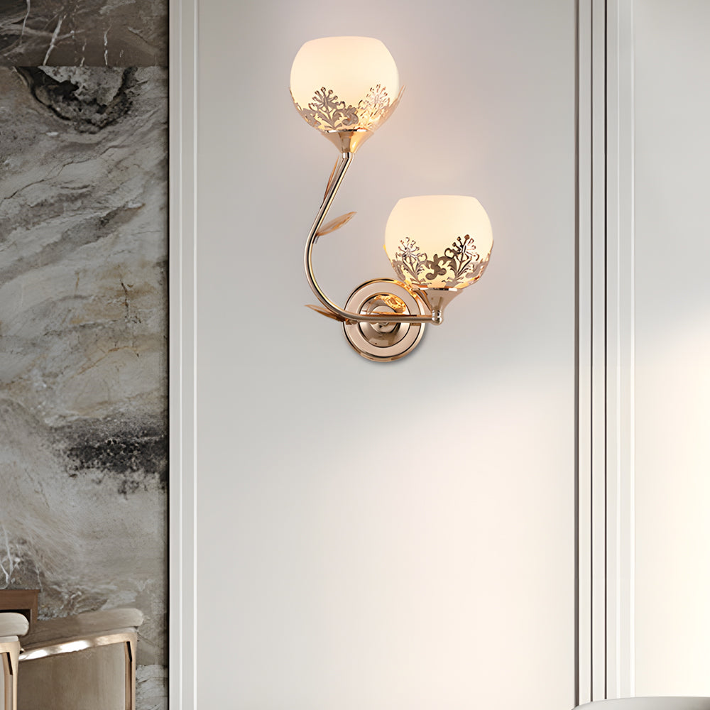 Gold floral wall sconce with frosted glass shade mounted on a decorative wall panel.