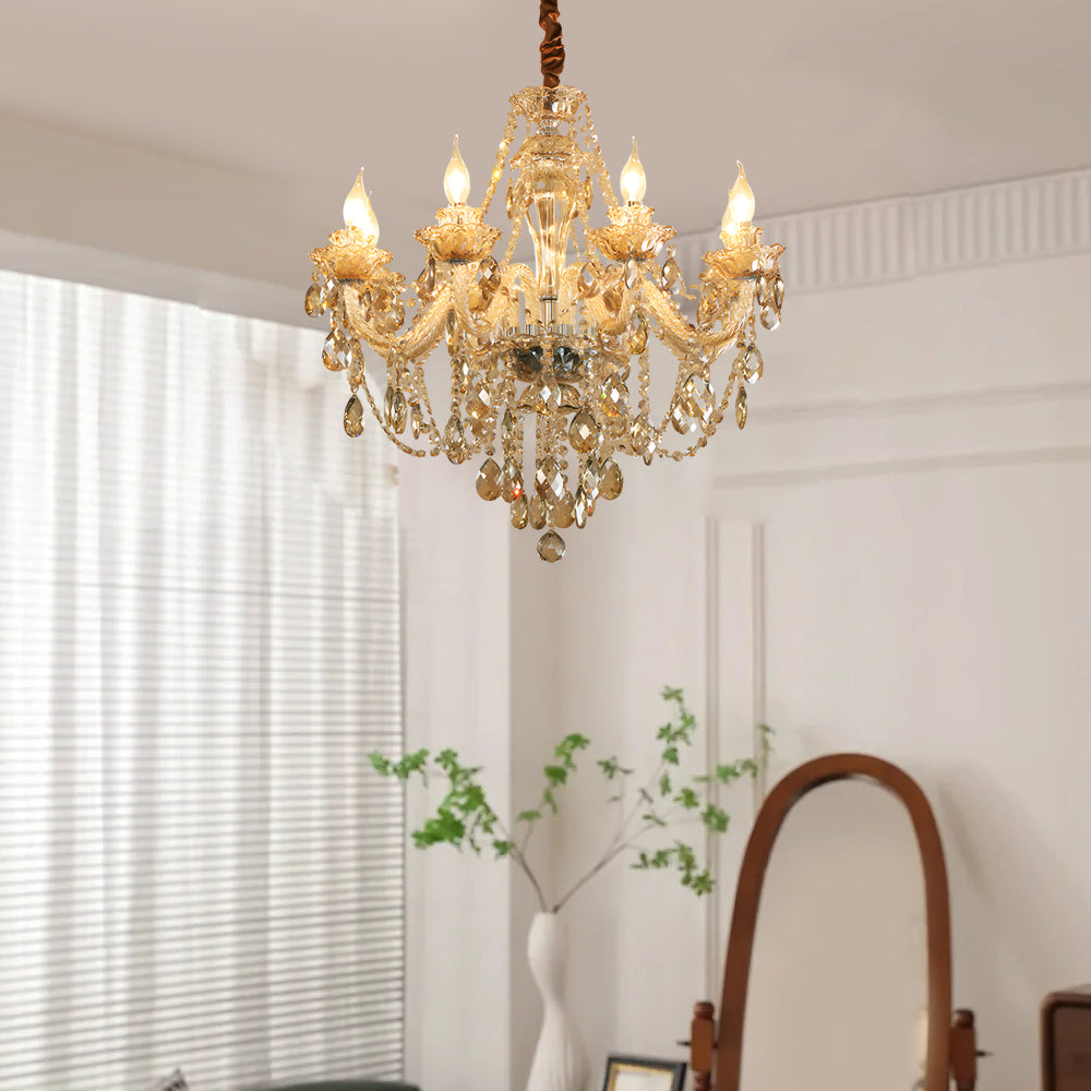 Gold glass candlelight chandelier shown hanging in front of white curtains in a bright room.