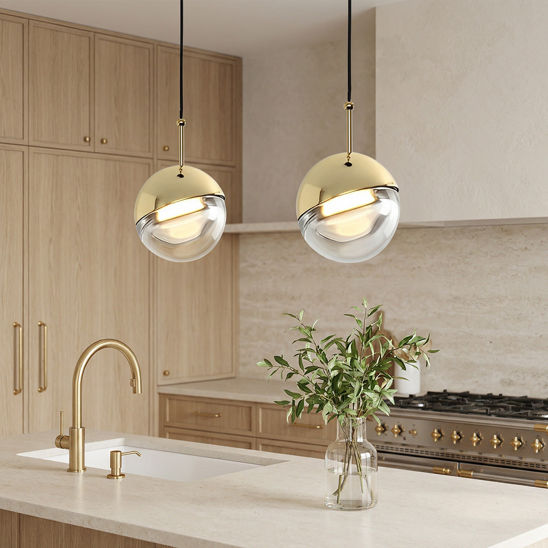 Two modern gold globe pendant lights with clear glass bottoms over a kitchen island marble top.