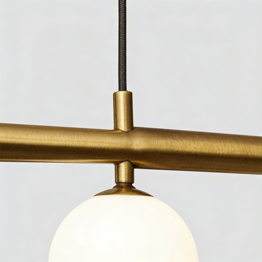 Close-up detail of gold linear pendant light metal finish and globe bulb.