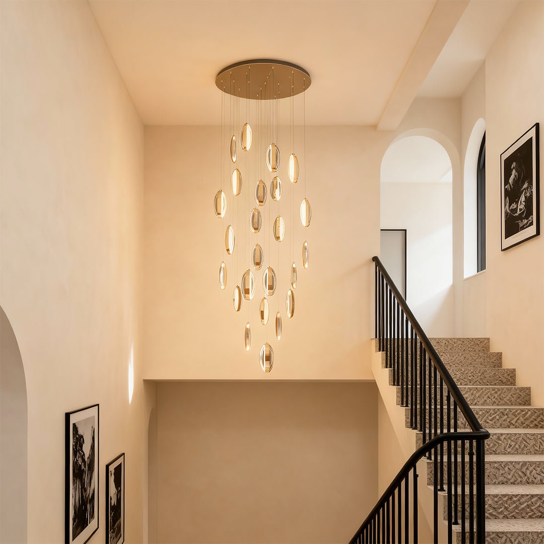 Gold modern chandelier suspended in bright hallway with neutral walls and modern architectural staircase railings