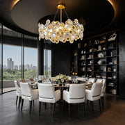 Gold modern chandelier illuminating formal dining room with marble table and city skyline views through floor-to-ceiling windows
