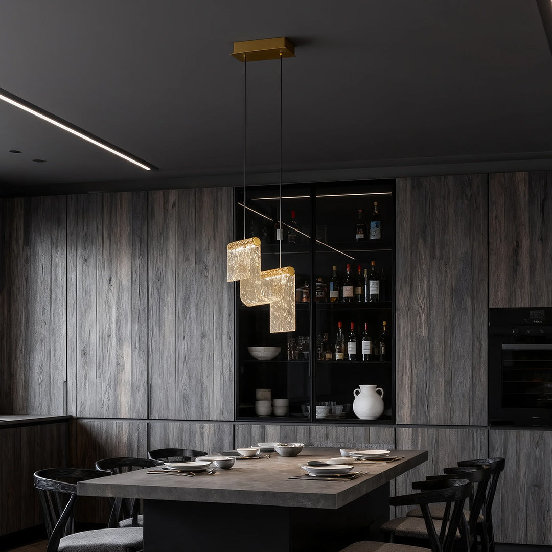 Gold pendant island light illuminating dark sophisticated dining room with grey concrete walls and black table