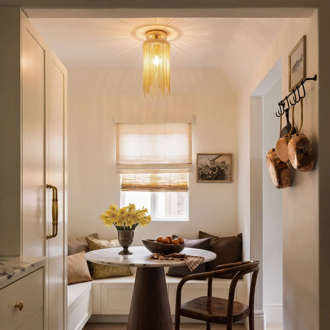 Gold tassel chandelier flush mount above a cozy breakfast nook in a bright cream hallway.