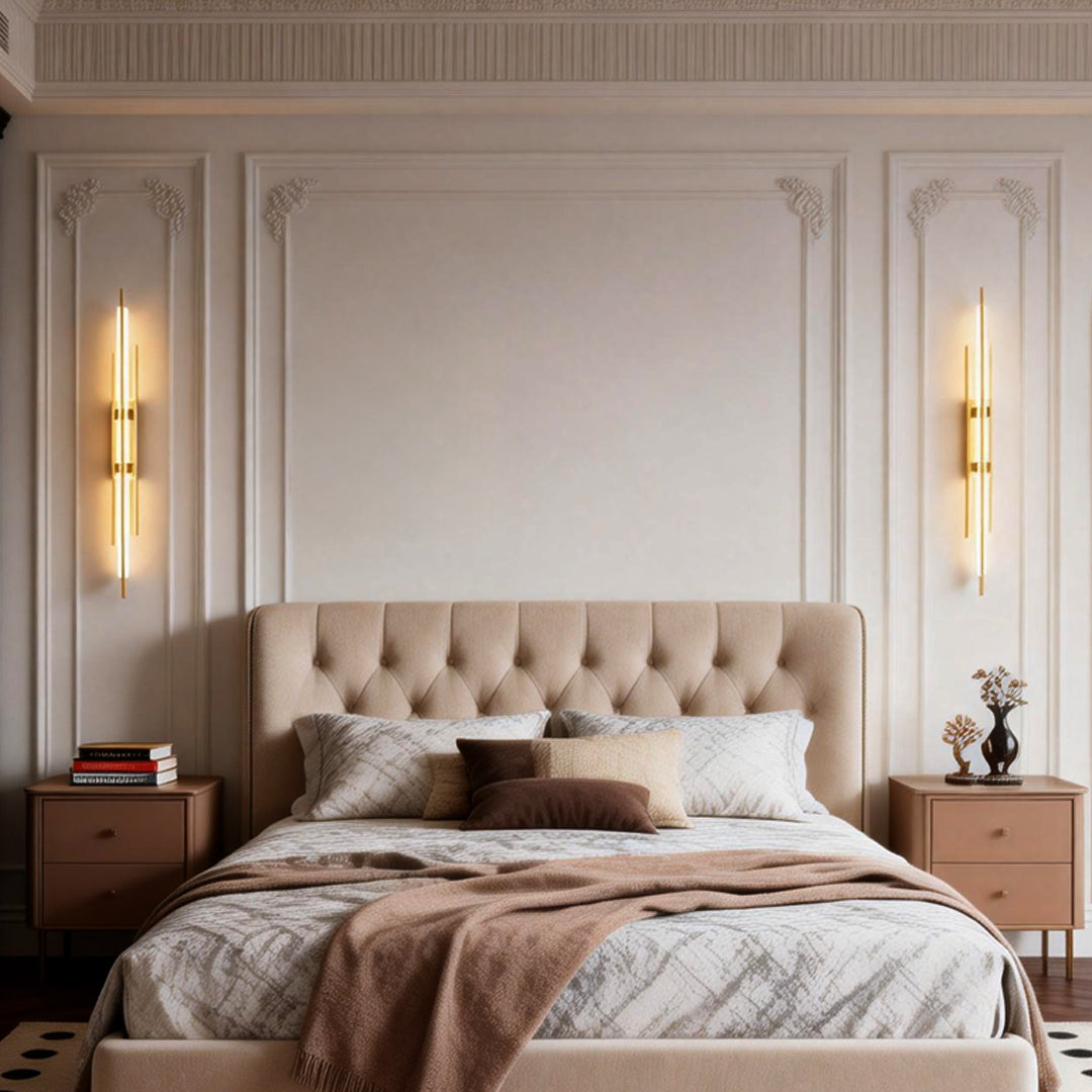 Gold tube wall sconce mounted on bedroom wall beside upholstered bed.