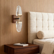 Gold wall light creating warm glow beside upholstered bed in elegant bedroom with rich wood architectural details