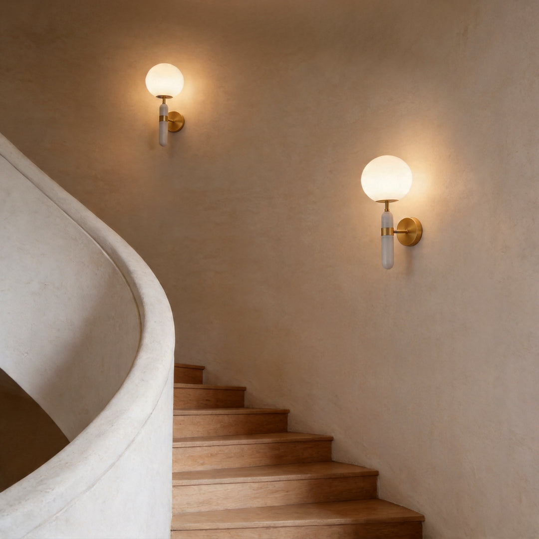 Two gold wall sconce lighting fixtures illuminating a curved minimalist staircase at night.
