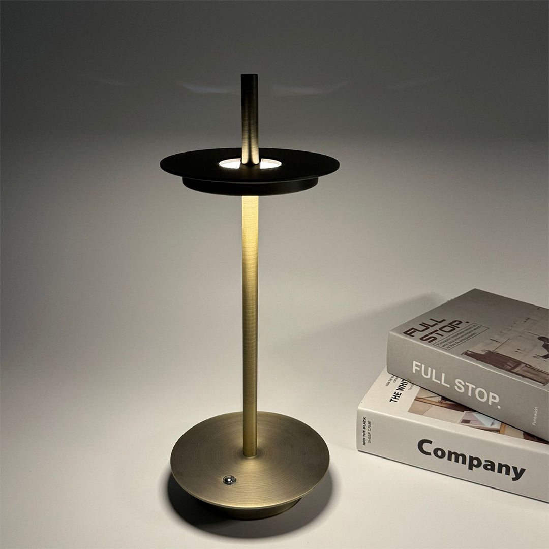 Dimmable table lamp with golden finish positioned next to books creating warm reading light