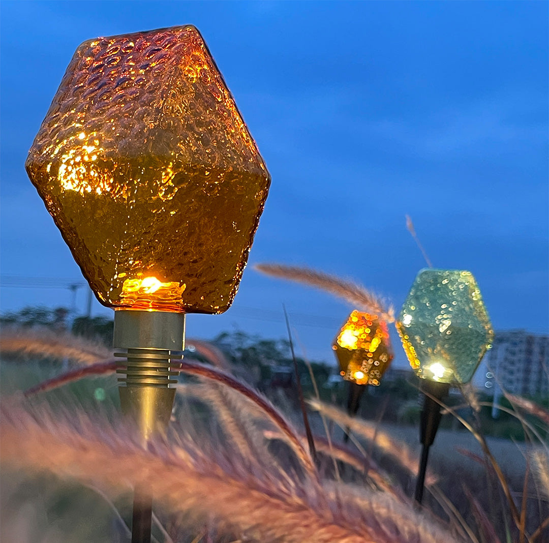Golden glowing globe stake lighting a garden field, ideal for landscape lighting pathway enhancement.