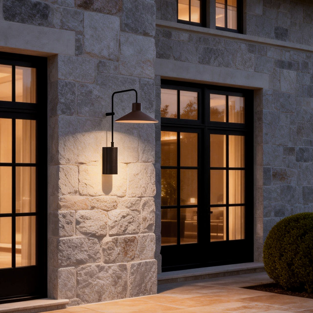 Gooseneck wall lamp mounted on a stone exterior wall, casting warm light beside a classic window entrance.