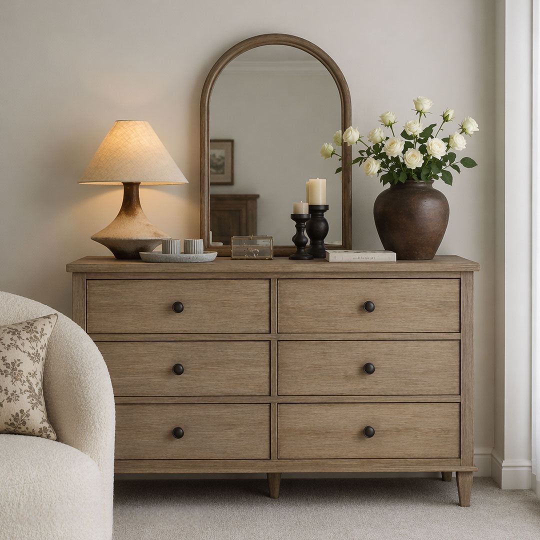 Gray ceramic table lamp displayed on a light wood dresser beneath an arched mirror with decorative accents.