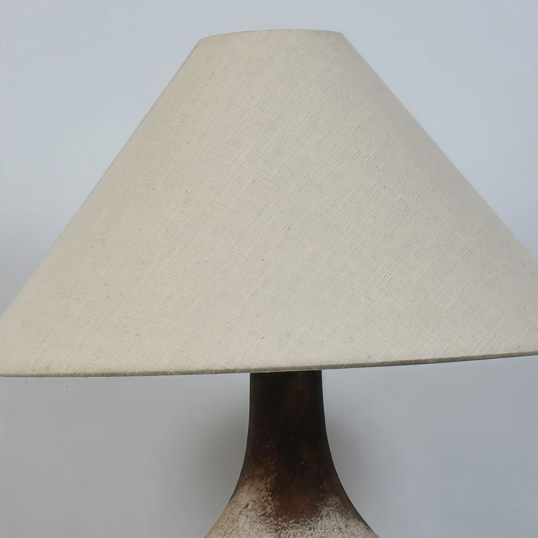 Close-up of a gray ceramic table lamp with a tapered fabric shade and dark textured ceramic base.
