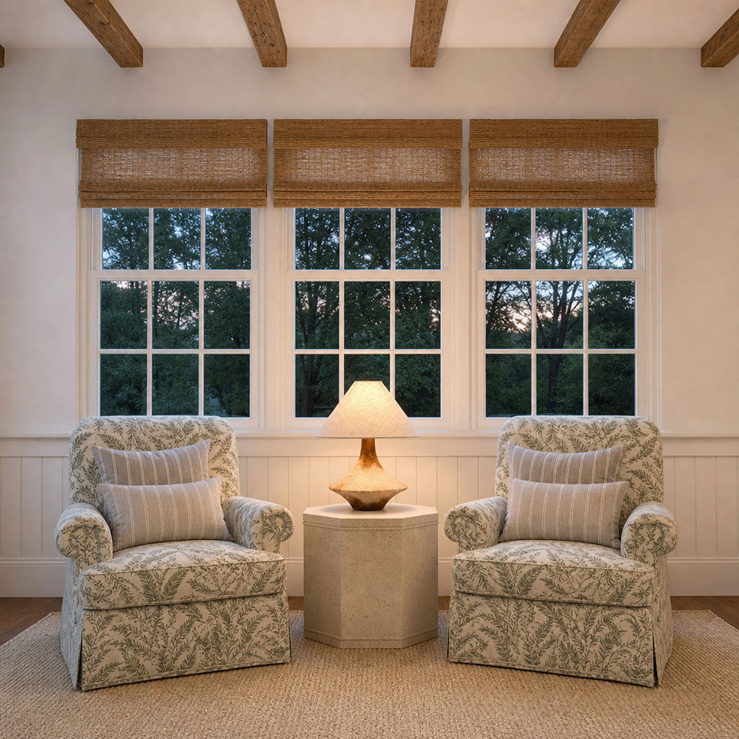 Gray ceramic table lamp centered between two upholstered armchairs in a bright sitting area with large windows.
