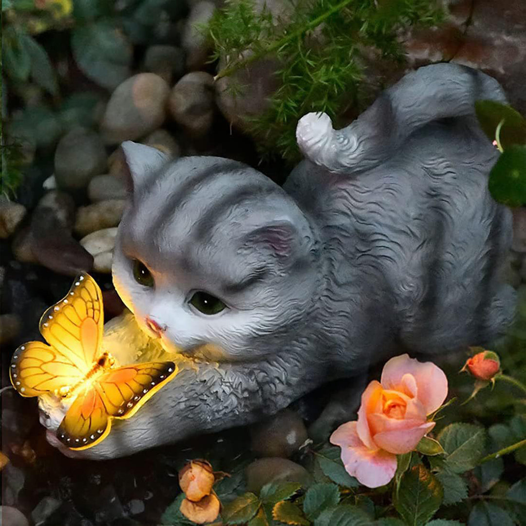 Gray kitten figurine with illuminated butterfly among decorative stones and small flowers