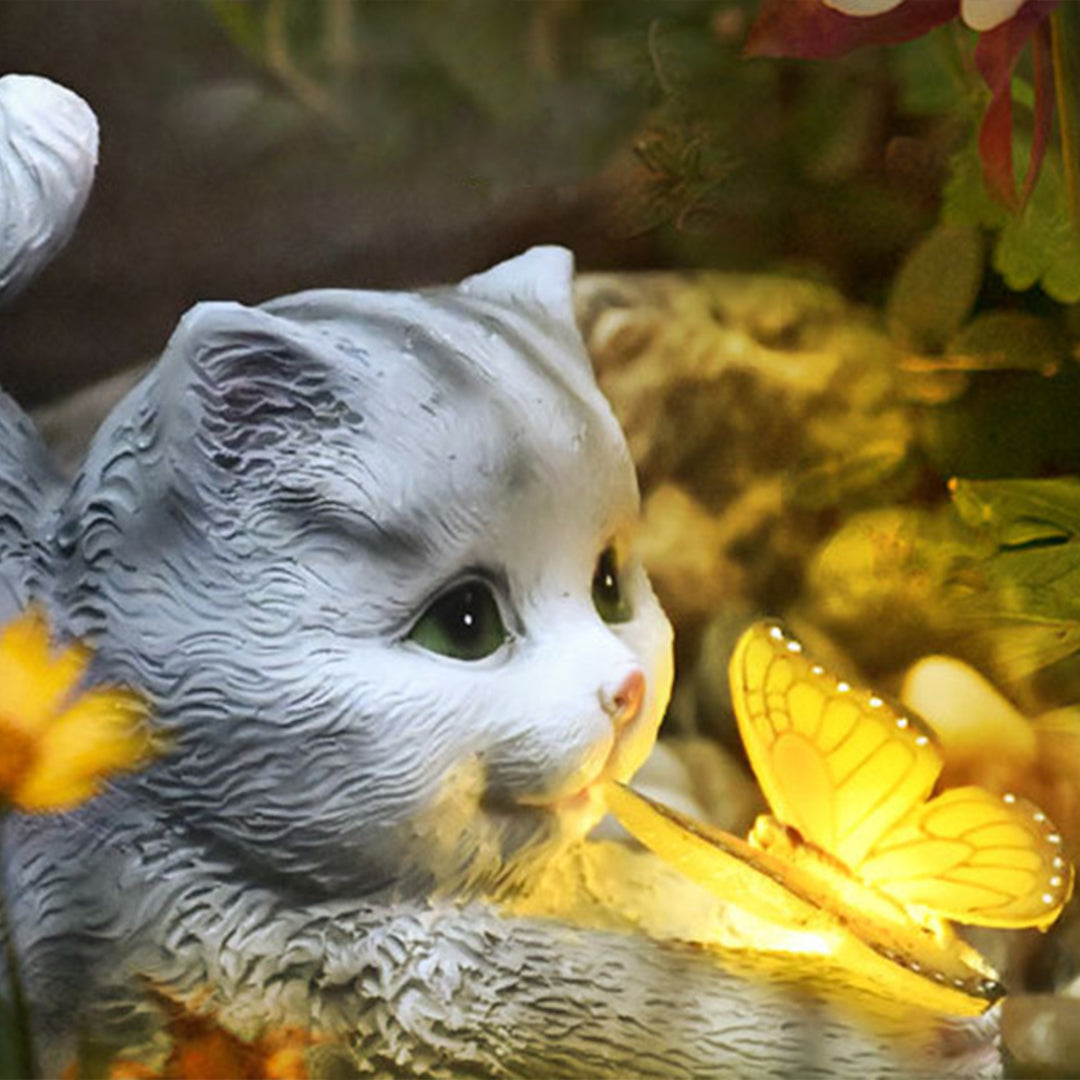 Gray kitten with bright yellow illuminated butterfly creating magical garden lighting effect