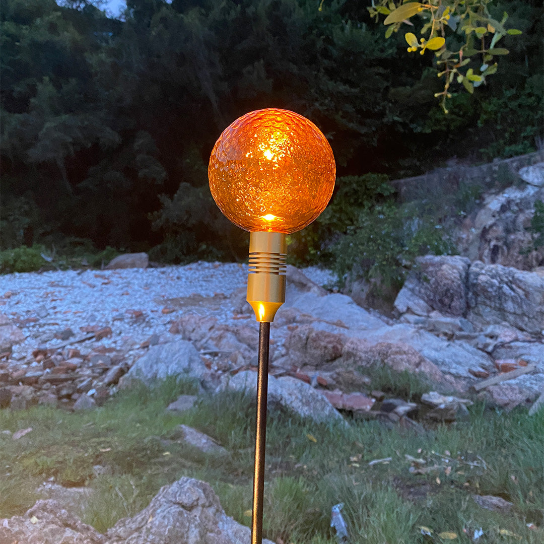 Green crackle-glass globe stake lights placed among plants, enhancing natural path landscape lighting.