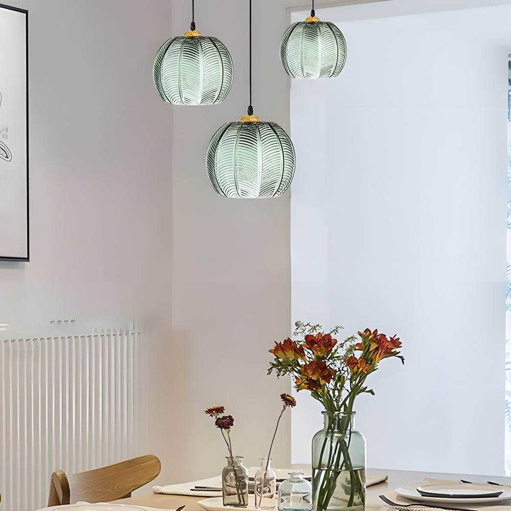 Three green glass pendant lights hanging at different heights over a dining table.