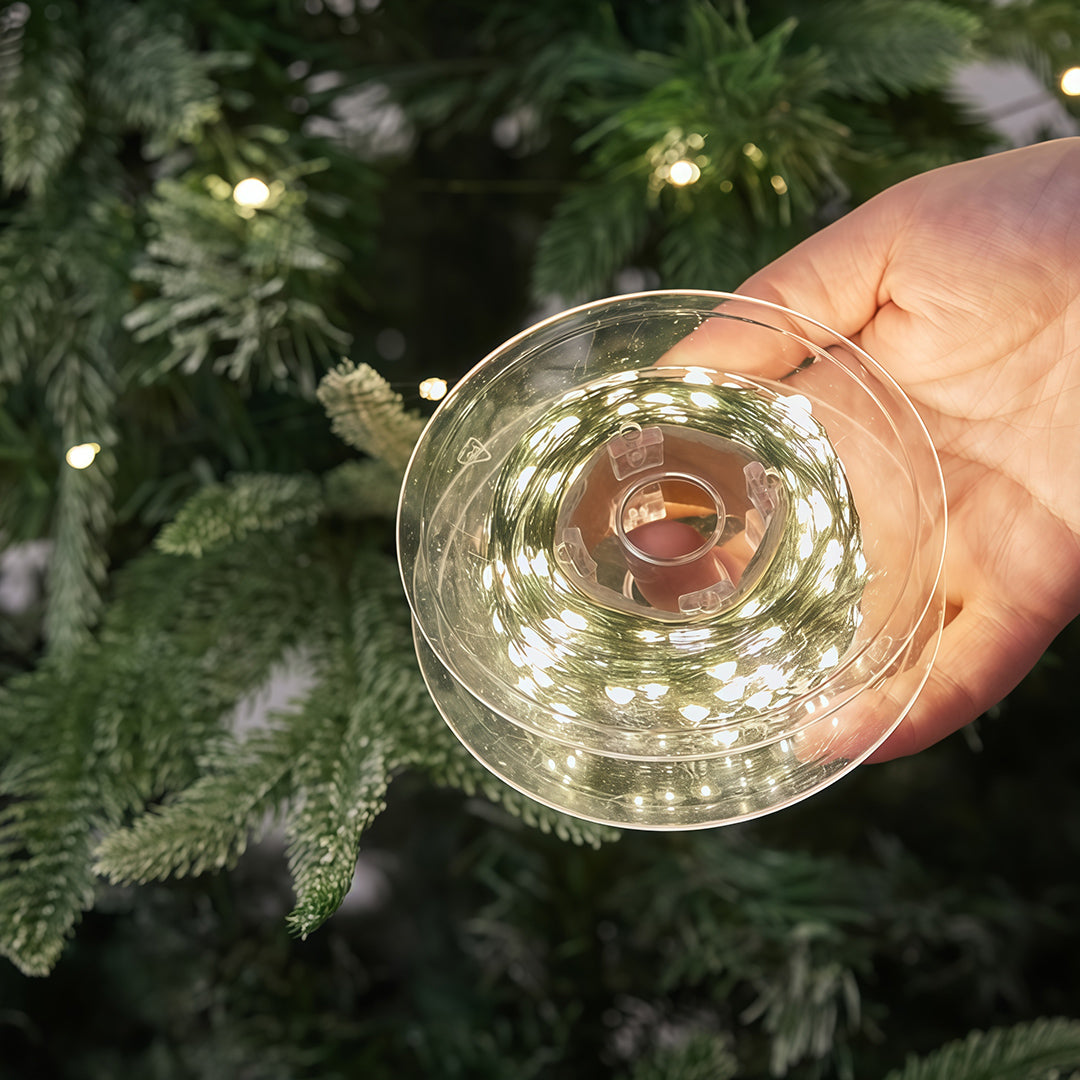Hand holding a transparent reel with green-wire Christmas string lights ready for installation.