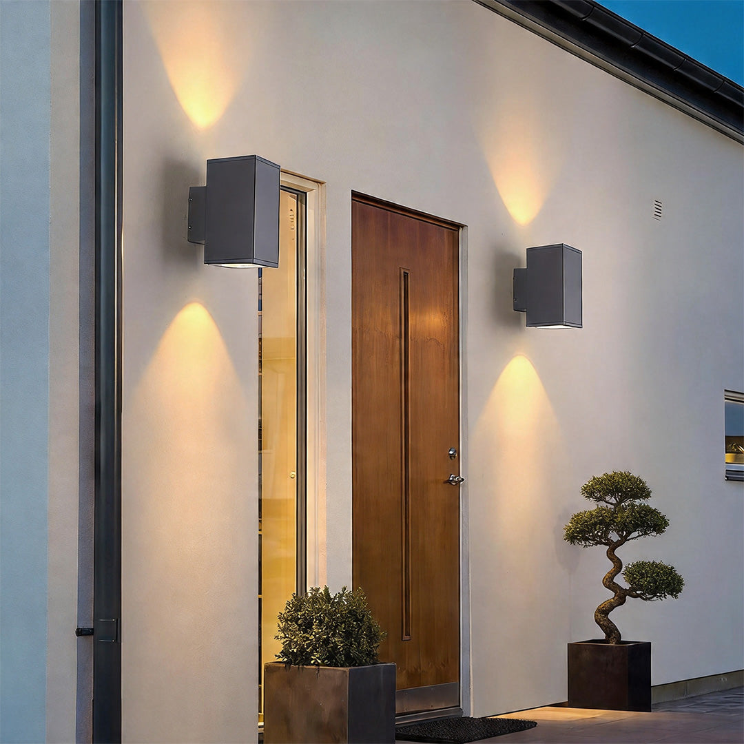 Grey wall sconce up and down light fixtures illuminating a modern white home entrance doorway.