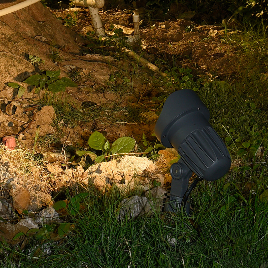 Small outdoor ground light fixture positioned among natural rock and vegetation landscape