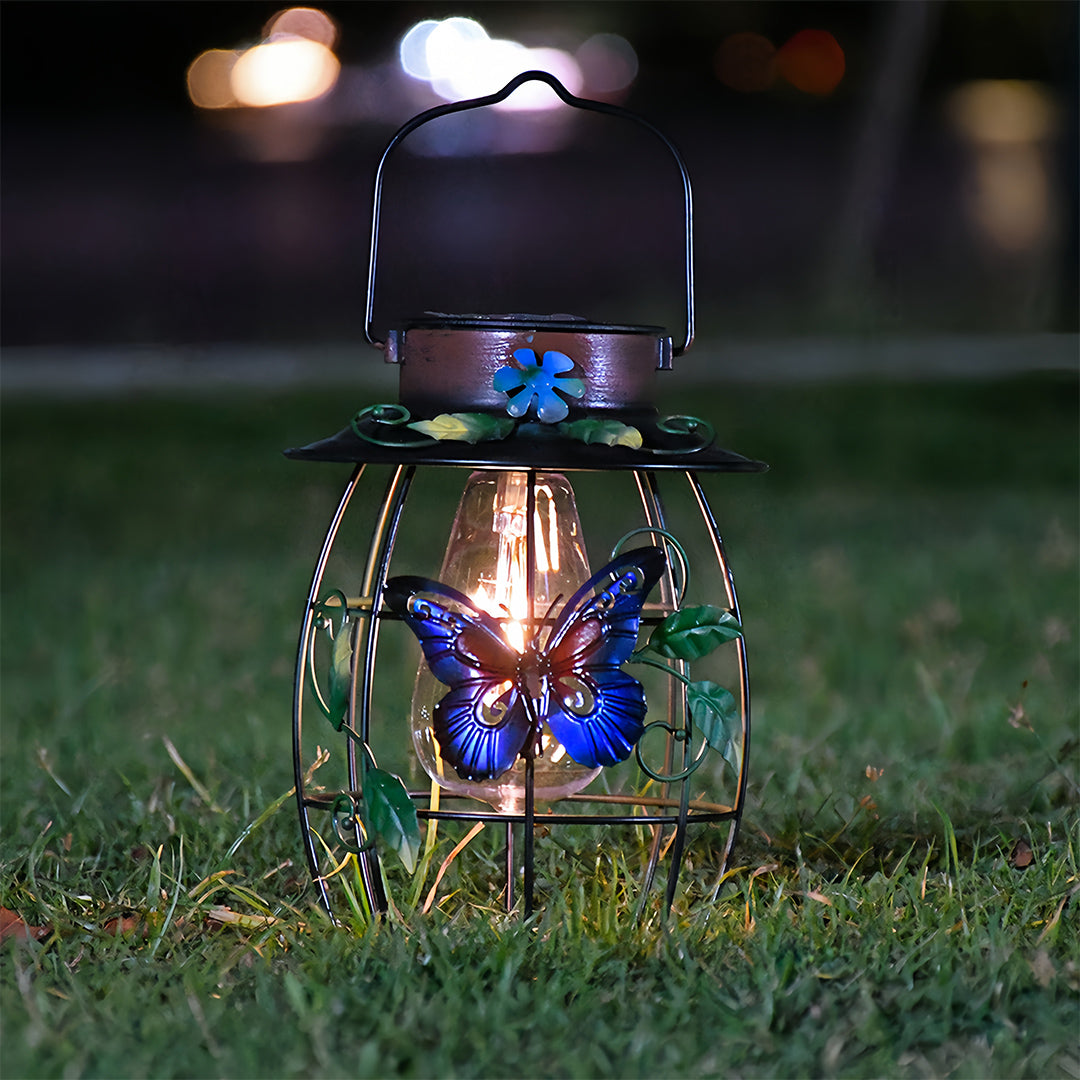 Ground placement of a lit iron outdoor lanterns with blue butterfly at dusk in the garden grass.